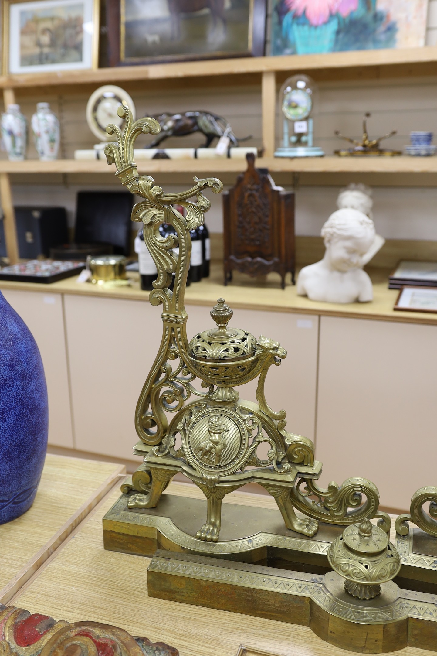 A pair of French bronze chenets, 19th century, with ornate decoration and cherub cartouche, adjustable curb, 64 cms high